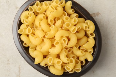 Photo of Raw horns pasta in bowl on gray textured table, top view