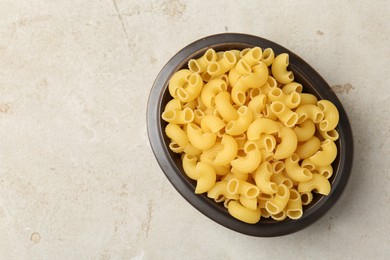 Photo of Raw horns pasta in bowl on gray textured table, top view. Space for text