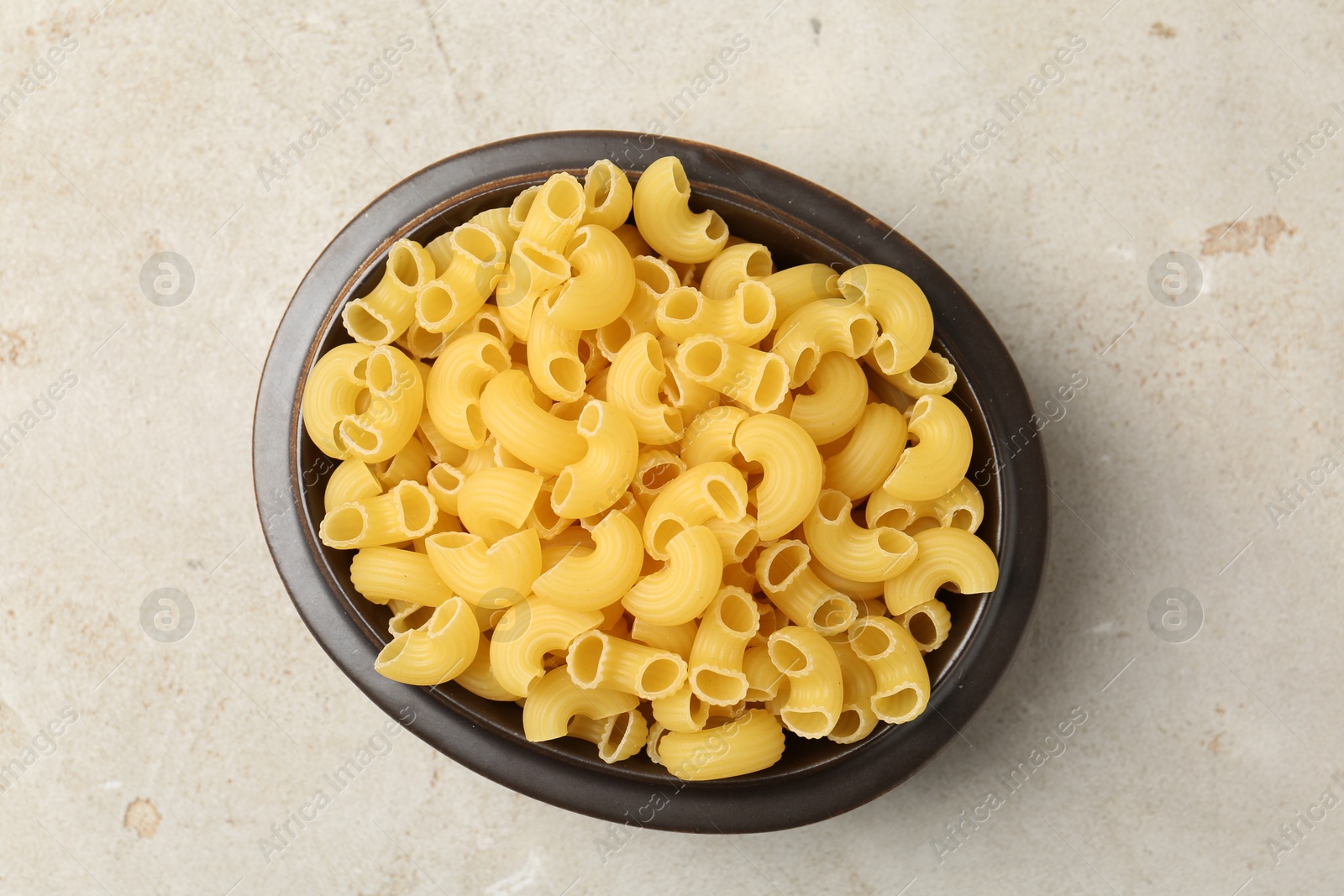 Photo of Raw horns pasta in bowl on gray textured table, top view