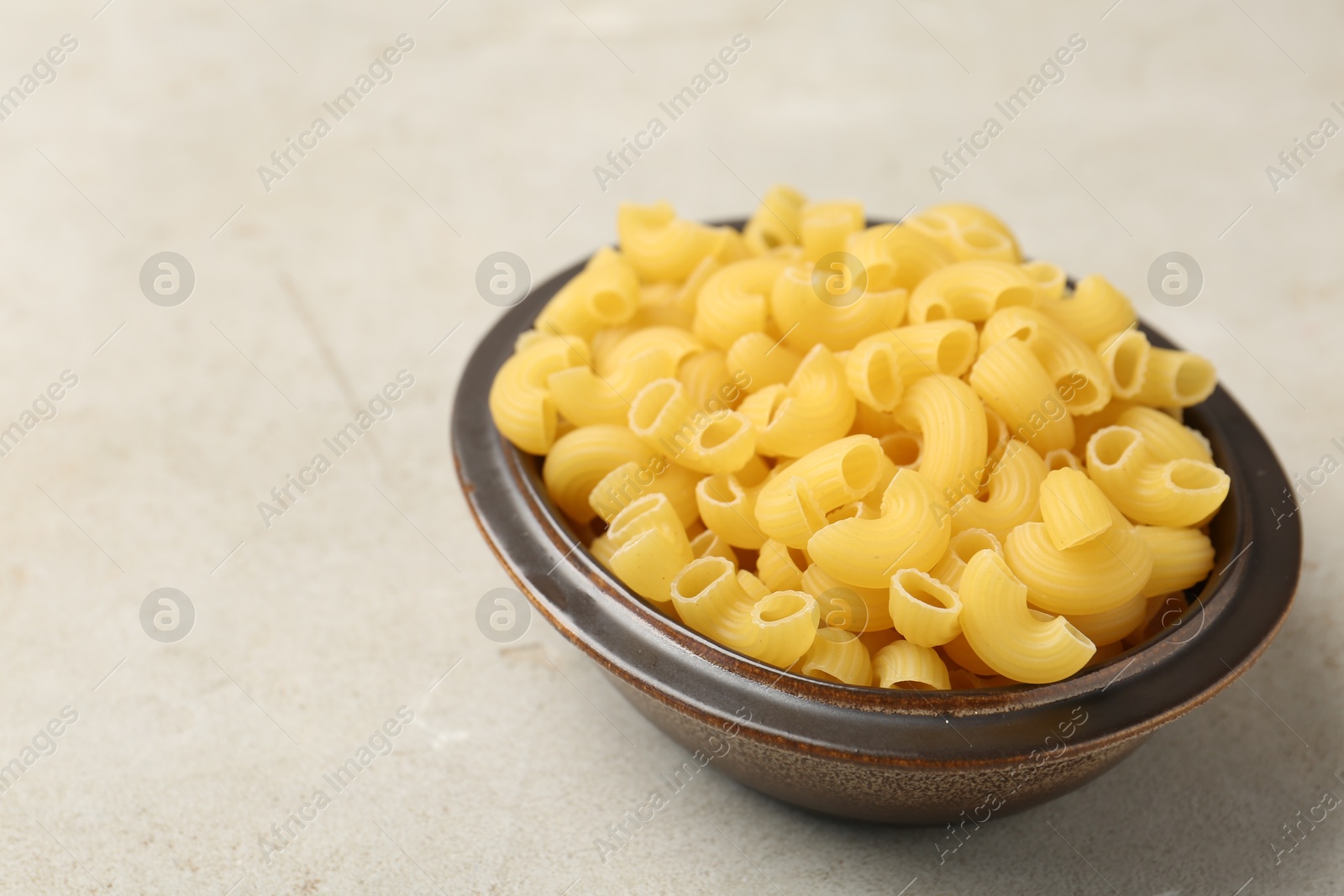 Photo of Raw horns pasta in bowl on gray textured table, closeup. Space for text