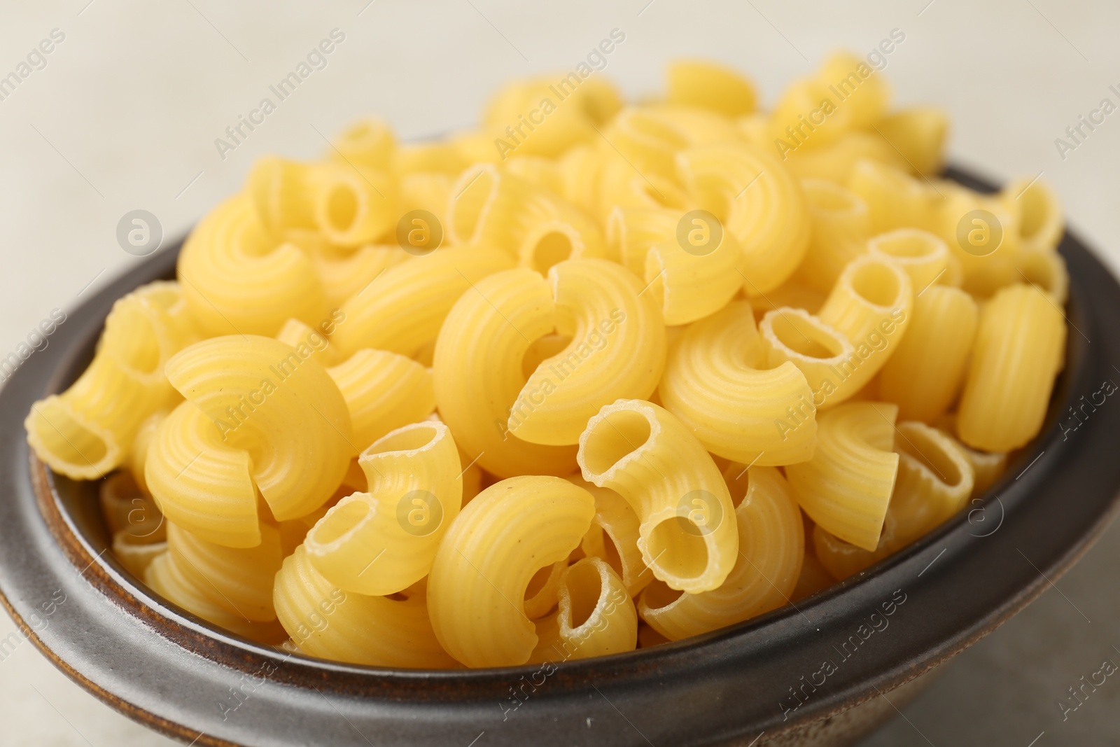 Photo of Raw horns pasta in bowl on gray table, closeup