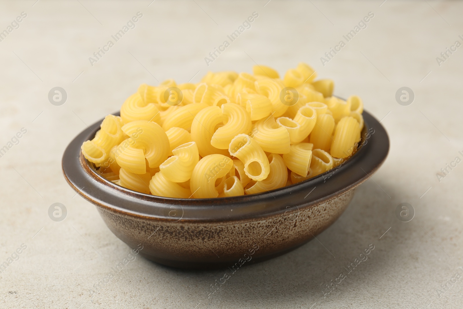 Photo of Raw horns pasta in bowl on gray textured table, closeup