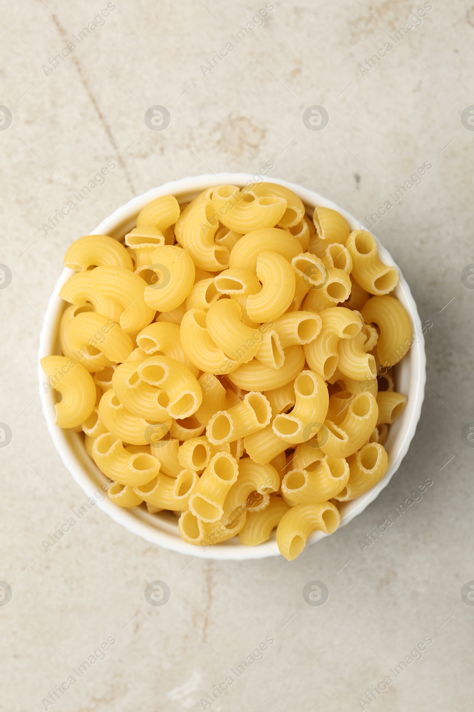 Photo of Raw horns pasta in bowl on gray textured table, top view