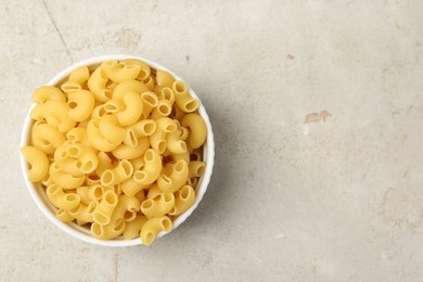 Photo of Raw horns pasta in bowl on gray textured table, top view. Space for text