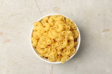 Photo of Raw horns pasta in bowl on gray textured table, top view