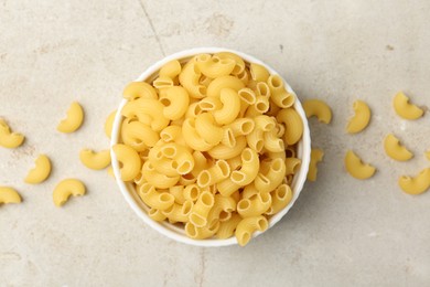 Photo of Raw horns pasta in bowl on gray textured table, top view