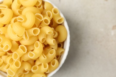 Photo of Raw horns pasta in bowl on gray textured table, top view. Space for text