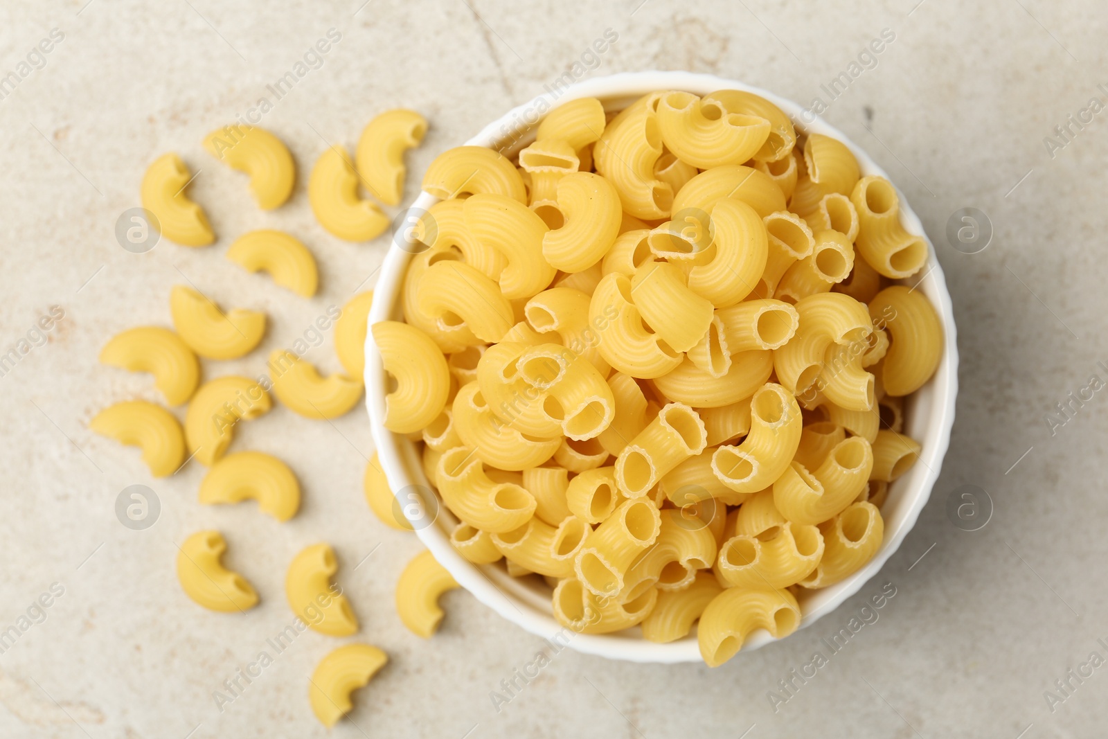 Photo of Raw horns pasta in bowl on gray textured table, top view