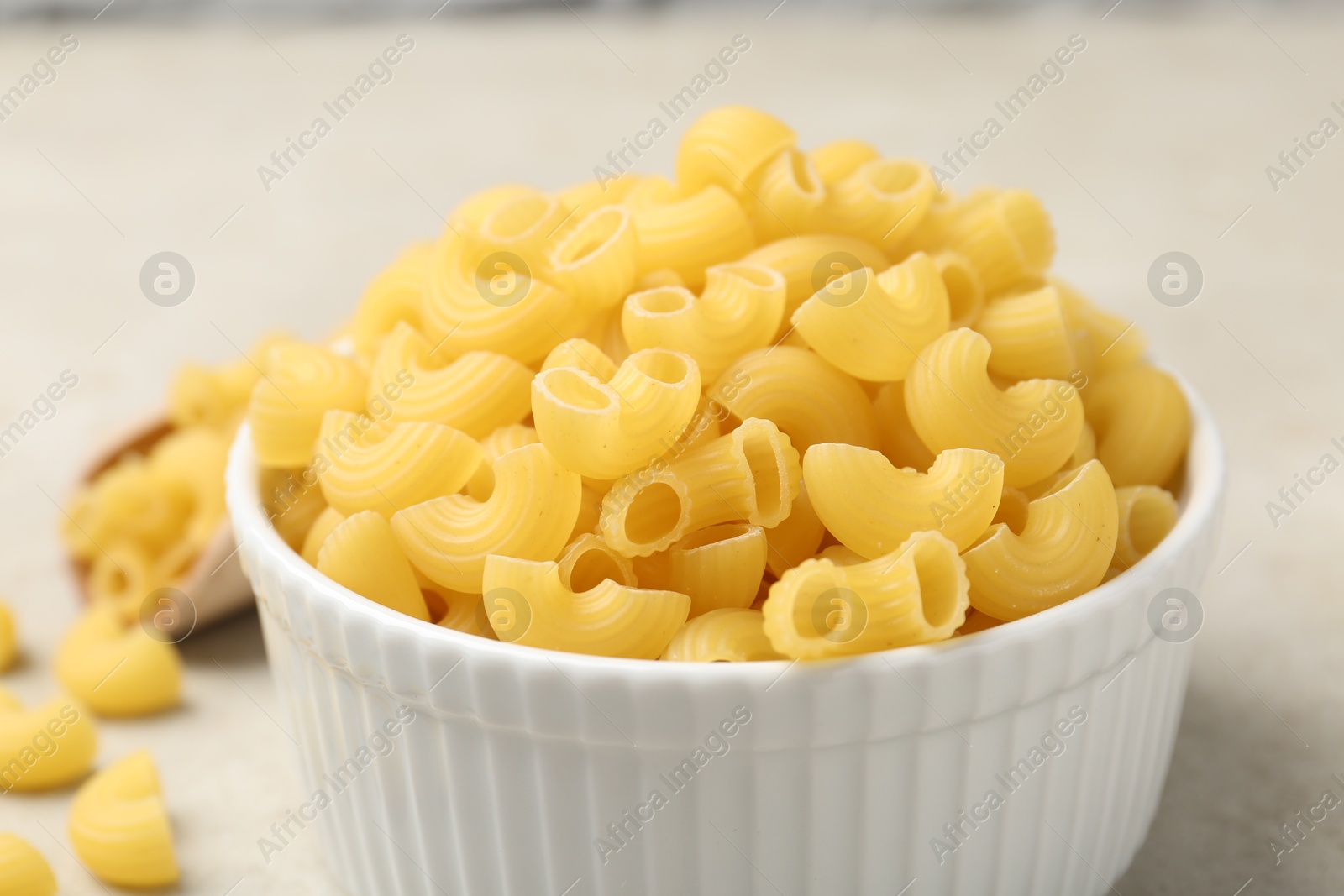 Photo of Raw horns pasta in bowl on gray table, closeup