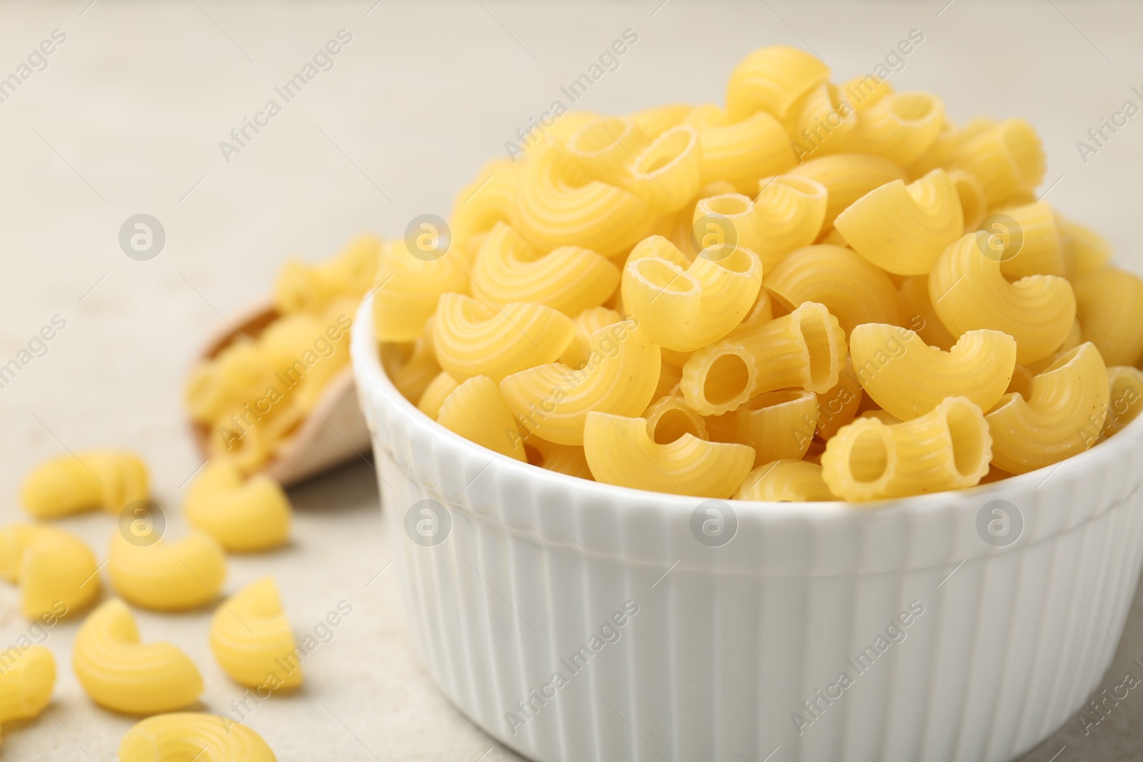 Photo of Raw horns pasta in bowl on gray table, closeup