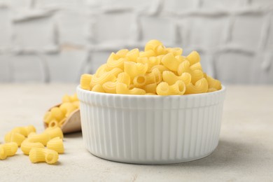 Photo of Raw horns pasta in bowl on gray textured table, closeup