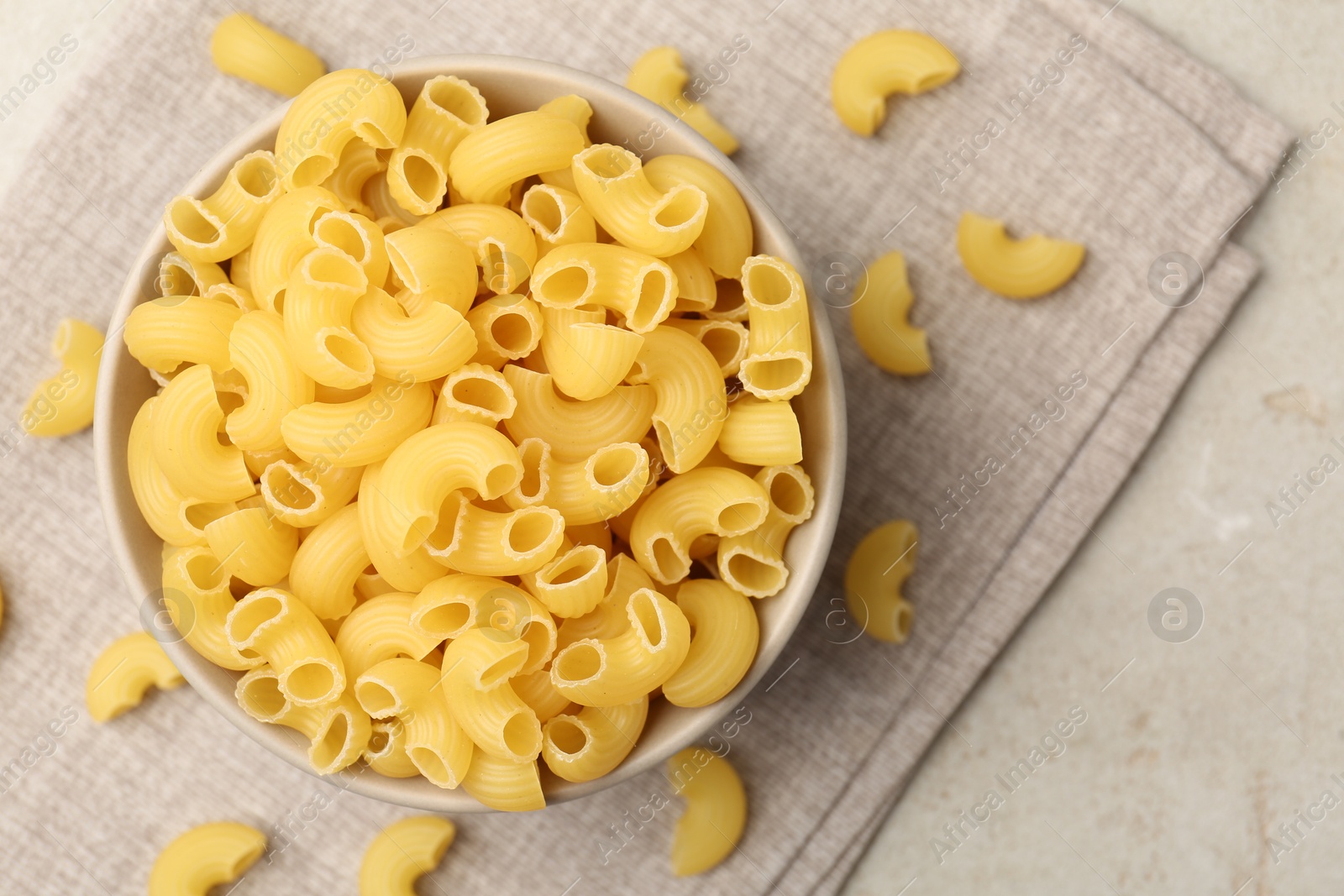 Photo of Raw horns pasta in bowl on gray table, top view