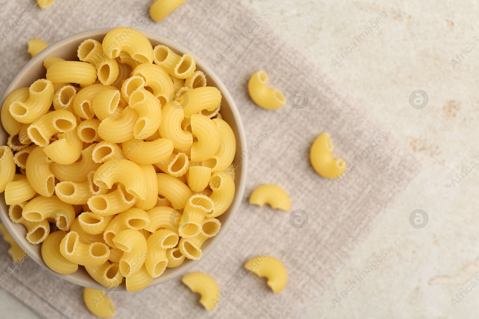 Photo of Raw horns pasta in bowl on gray textured table, top view. Space for text