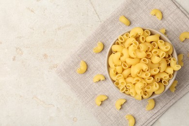 Photo of Raw horns pasta in bowl on gray textured table, top view. Space for text