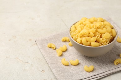 Photo of Raw horns pasta in bowl on gray textured table, space for text