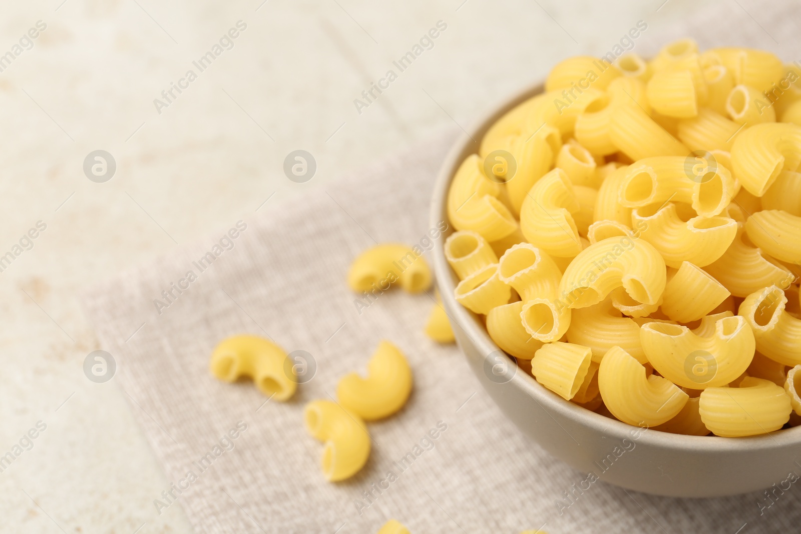 Photo of Raw horns pasta in bowl on gray table, closeup. Space for text