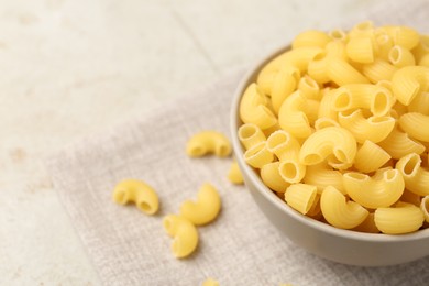 Photo of Raw horns pasta in bowl on gray table, closeup. Space for text