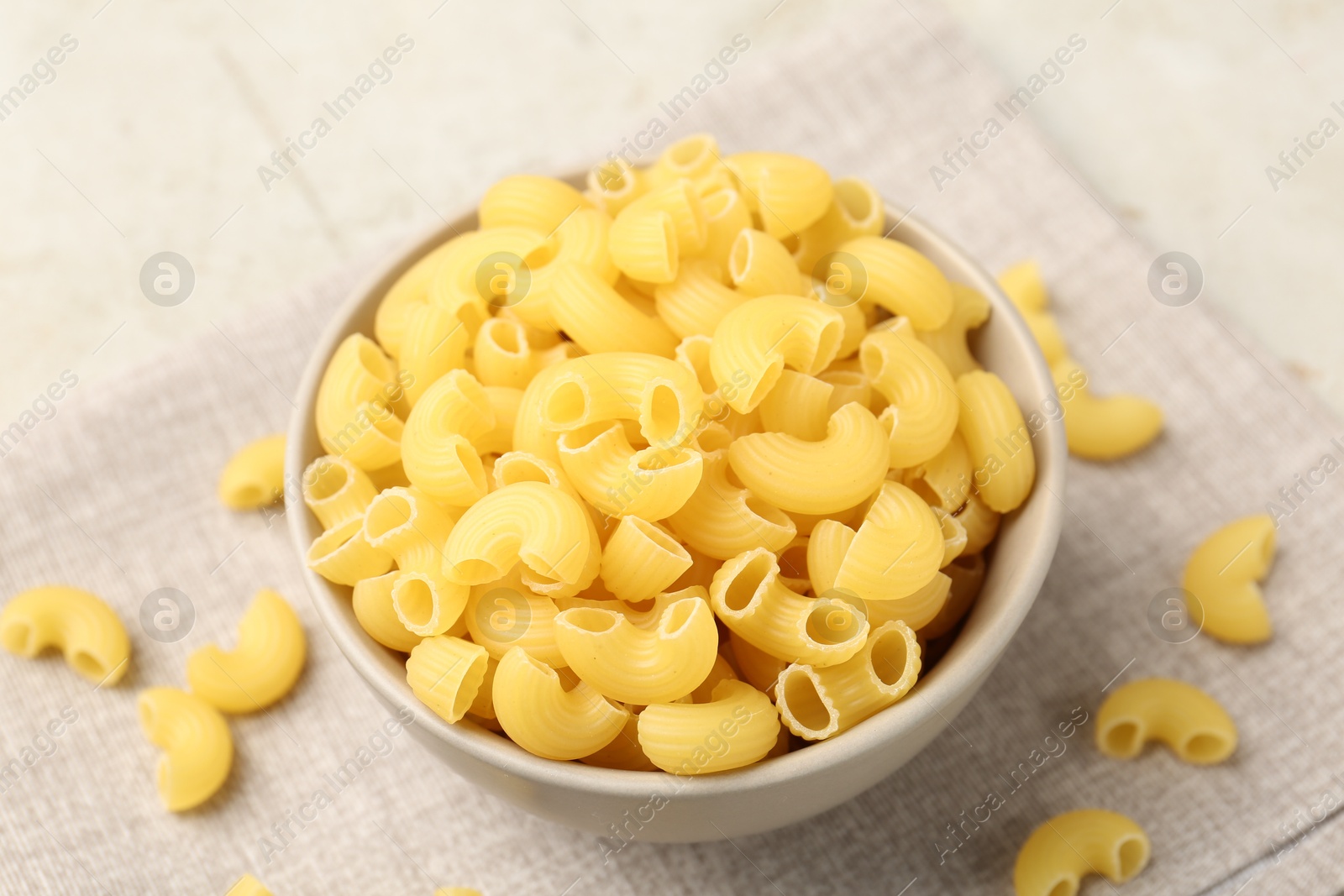 Photo of Raw horns pasta in bowl on gray table, closeup