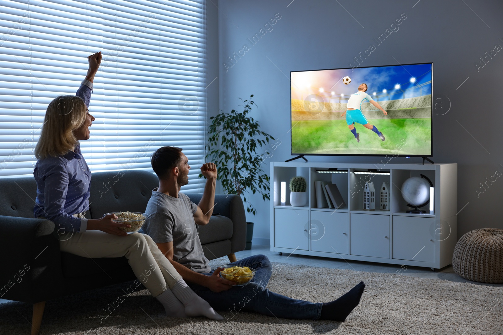 Image of Couple watching soccer game on TV set at home