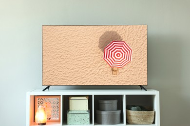 Image of TV set with umbrella amongst sandy beach on screen in room