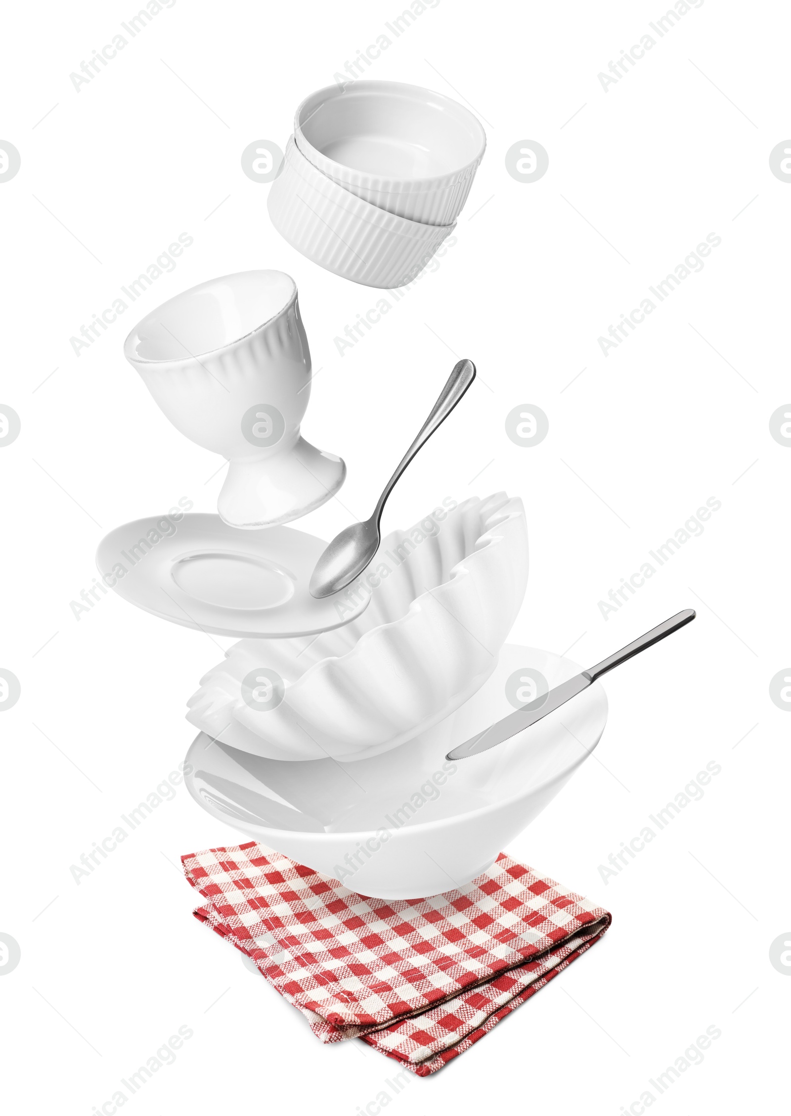 Image of Clean dishware and silverware flying over red checkered napkin on white background