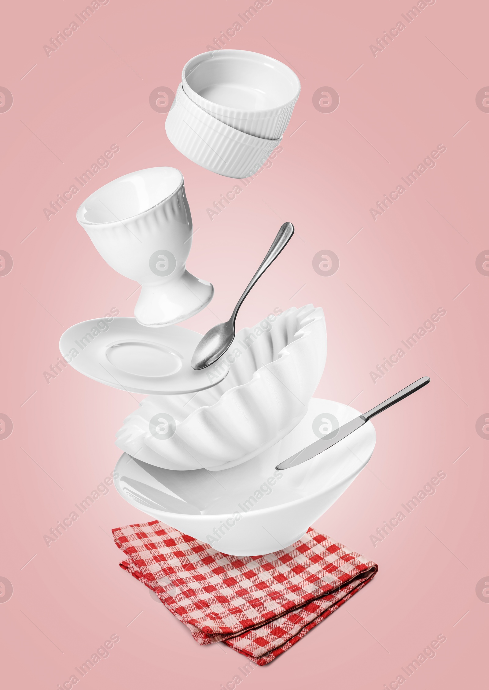 Image of Clean dishware and silverware flying over red checkered napkin on pink background