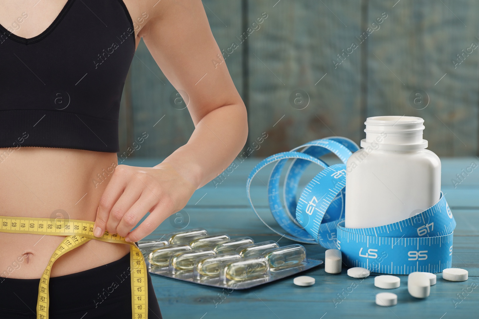 Image of Weight loss. Slim woman measuring her waist with tape and pills, closeup