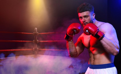 Image of Boxer training on boxing ring in color lights and smoke. Space for text