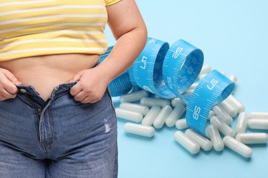 Image of Weight loss. Overweight woman and pills with measuring tape on light blue background, closeup