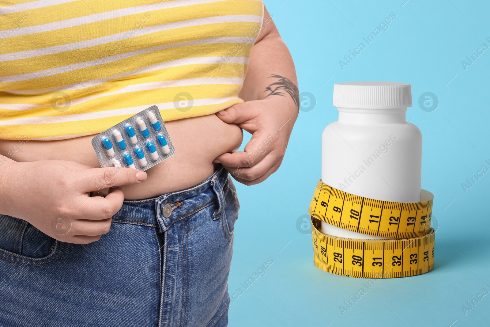 Image of Weight loss. Overweight woman with pills and measuring tape on light blue background, closeup