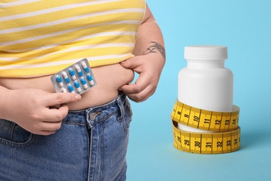 Image of Weight loss. Overweight woman with pills and measuring tape on light blue background, closeup