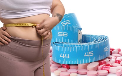 Image of Weight loss. Overweight woman measuring her waist with tape and pills on white background, closeup