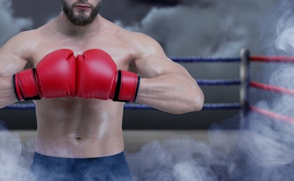 Image of Boxer wearing red gloves on boxing ring in smoke, closeup. Space for text