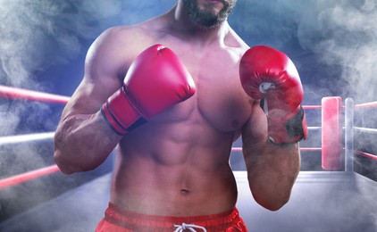 Image of Boxer wearing red gloves on boxing ring in smoke, closeup