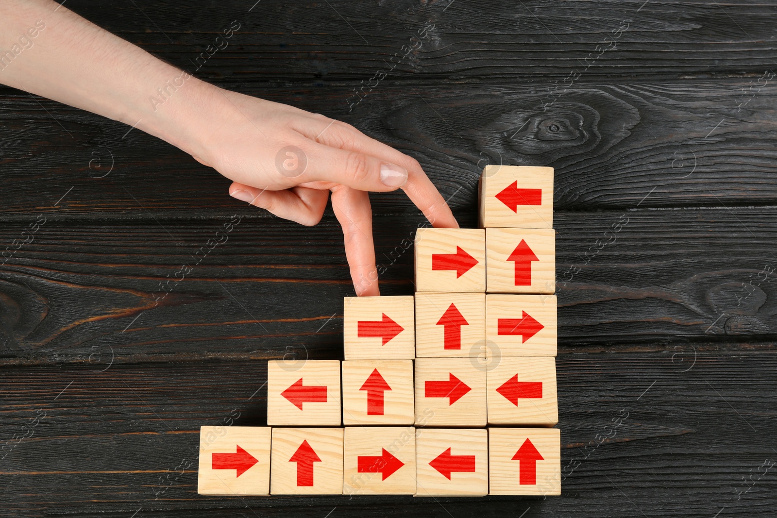 Image of Stairs made of cubes with arrows and woman's hand stepping up, wooden background