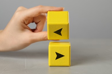 Image of Woman holding yellow cube with arrow at grey table, closeup