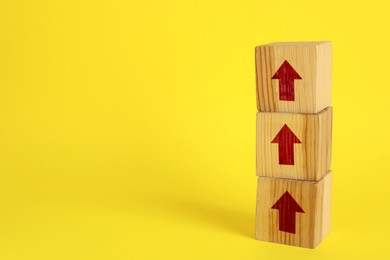 Image of Wooden cubes with red arrows on yellow background, space for text