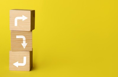 Image of Wooden cubes with arrows pointing in different directions on yellow background, space for text