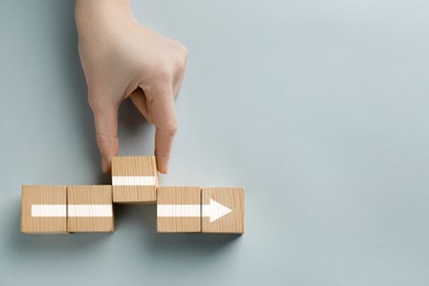 Image of Woman making arrow of cubes on grey background, top view. Space for text