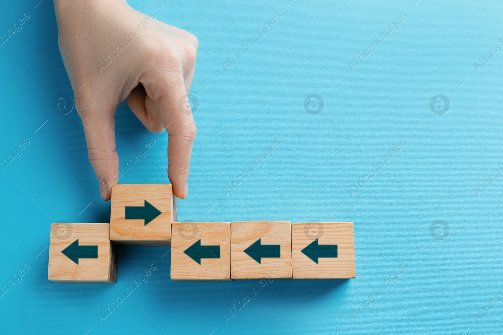 Image of Woman holding wooden cube with arrow on light blue background, top view. Space for text