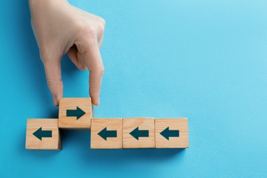 Image of Woman holding wooden cube with arrow on light blue background, top view. Space for text