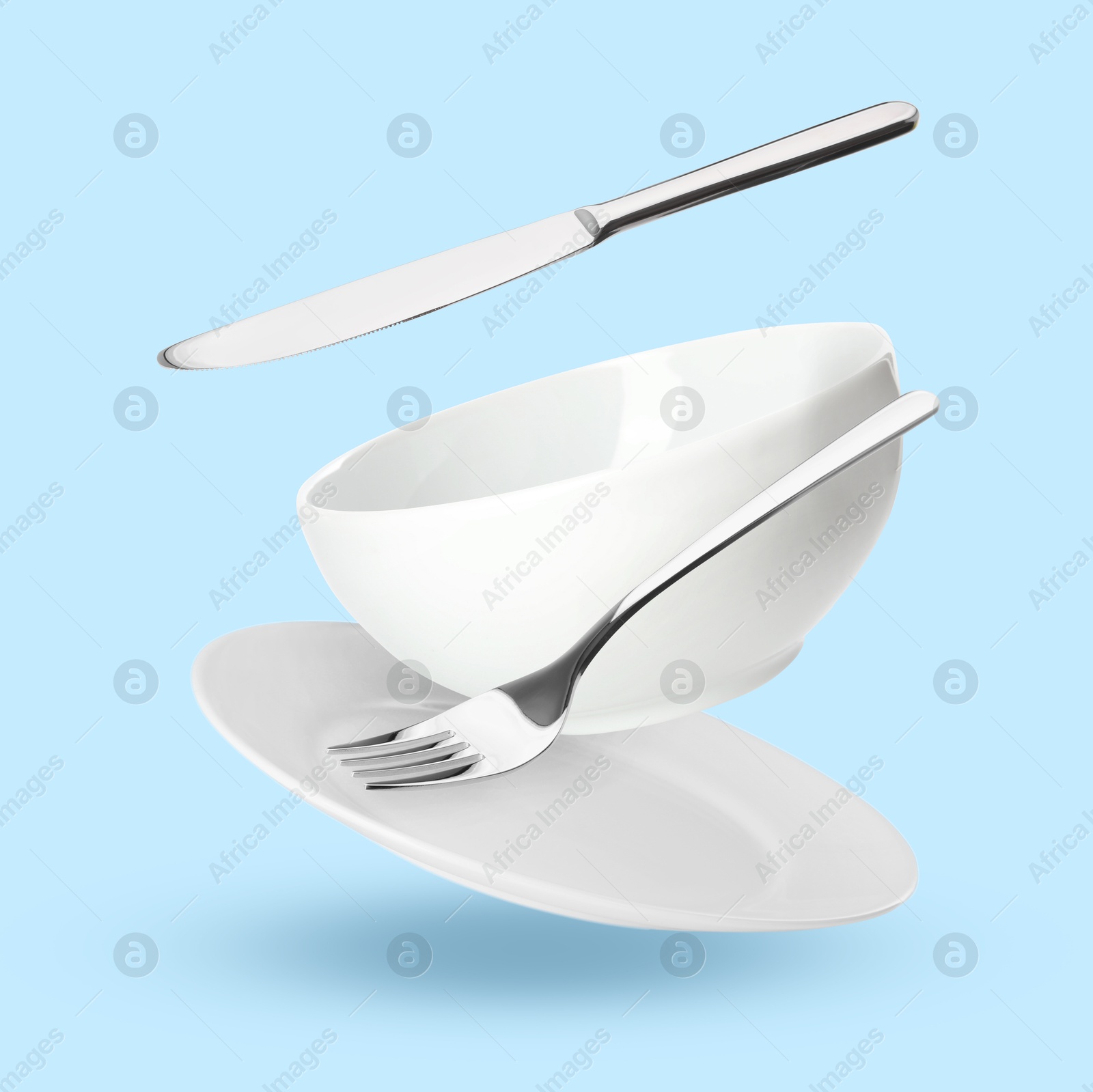 Image of Clean dishware and silverware flying on light blue background