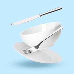 Image of Clean dishware and silverware flying on light blue background