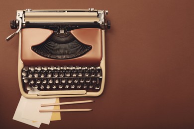 Image of Old vintage typewriter, paper and pencils on brown background, top view. Space for text