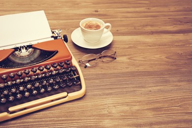 Image of Old typewriter with paper, cup of coffee and eyeglasses on wooden table, space for text