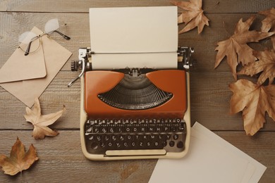 Image of Old vintage typewriter with paper and dry leaves on wooden table, top view