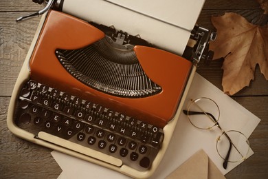 Image of Old vintage typewriter with paper, dry leaf and eyeglasses on wooden table, top view