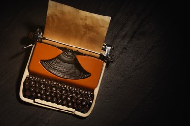Image of Old vintage typewriter with paper on black table, top view. Space for text