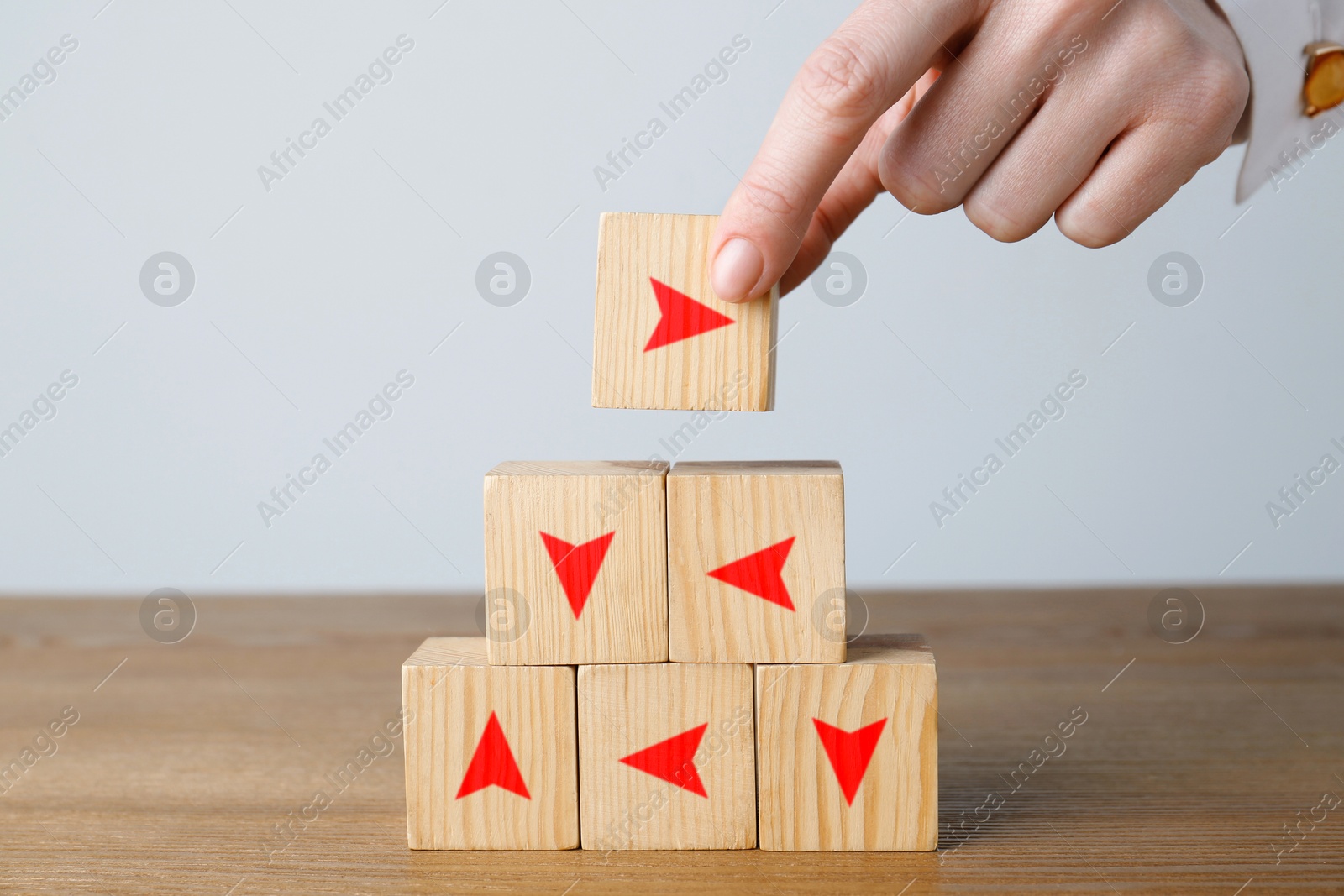 Image of Woman stacking cubes with arrows pointing in different directions at wooden table, closeup