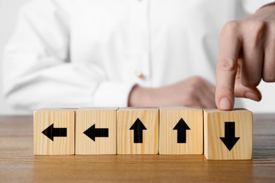 Image of Woman touching cube with black arrow at wooden table, closeup